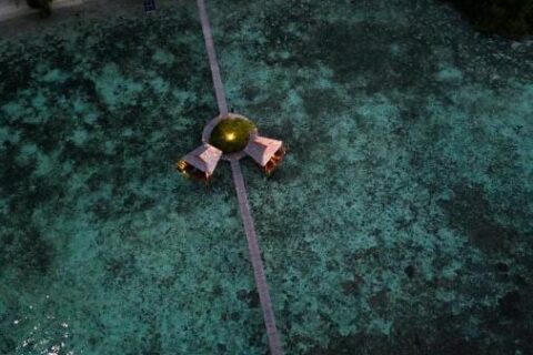 Vue aérienne de nuit d'une longue jetée en bois qui part de la plage, avec deux cabanes sur pilotis à mi-chemin