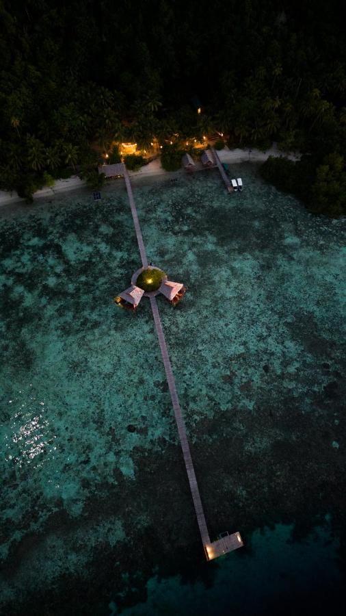 Vue aérienne de nuit d'une longue jetée en bois qui part de la plage, avec deux cabanes sur pilotis à mi-chemin