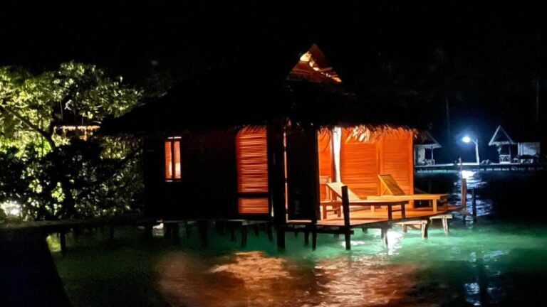 Un bungalow sur pilotis éclairé la nuit, avec des transats sur sa terrasse