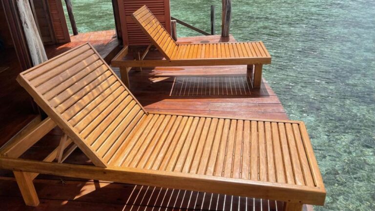 Deux transats en bois sur la terrasse d'un bungalow, au-dessus de l'eau claire