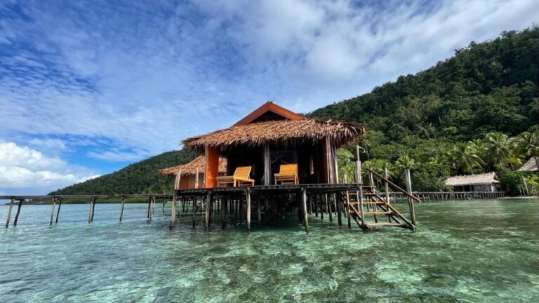 Un bungalow du Nyande Raja Ampat sur pilotis, au-dessus de l'eau claire, au pied d'une colline boisée