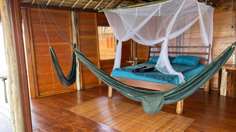 Une chambre en bois ouverte sur l'extérieur, avec un lit aux draps bleus sous moustiquaire et un hamac vert