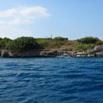 L'île de Pescador vue de la mer, couverte de buissons verts, son phare blanc au sommet et trois bancas de plongée amarrées au pied de la falaise