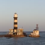 Le phare de Daedalus, une tour à bandes noires et blanches posée sur le récif, avec ses bâtiments et sa jetée métallique, au coucher du soleil