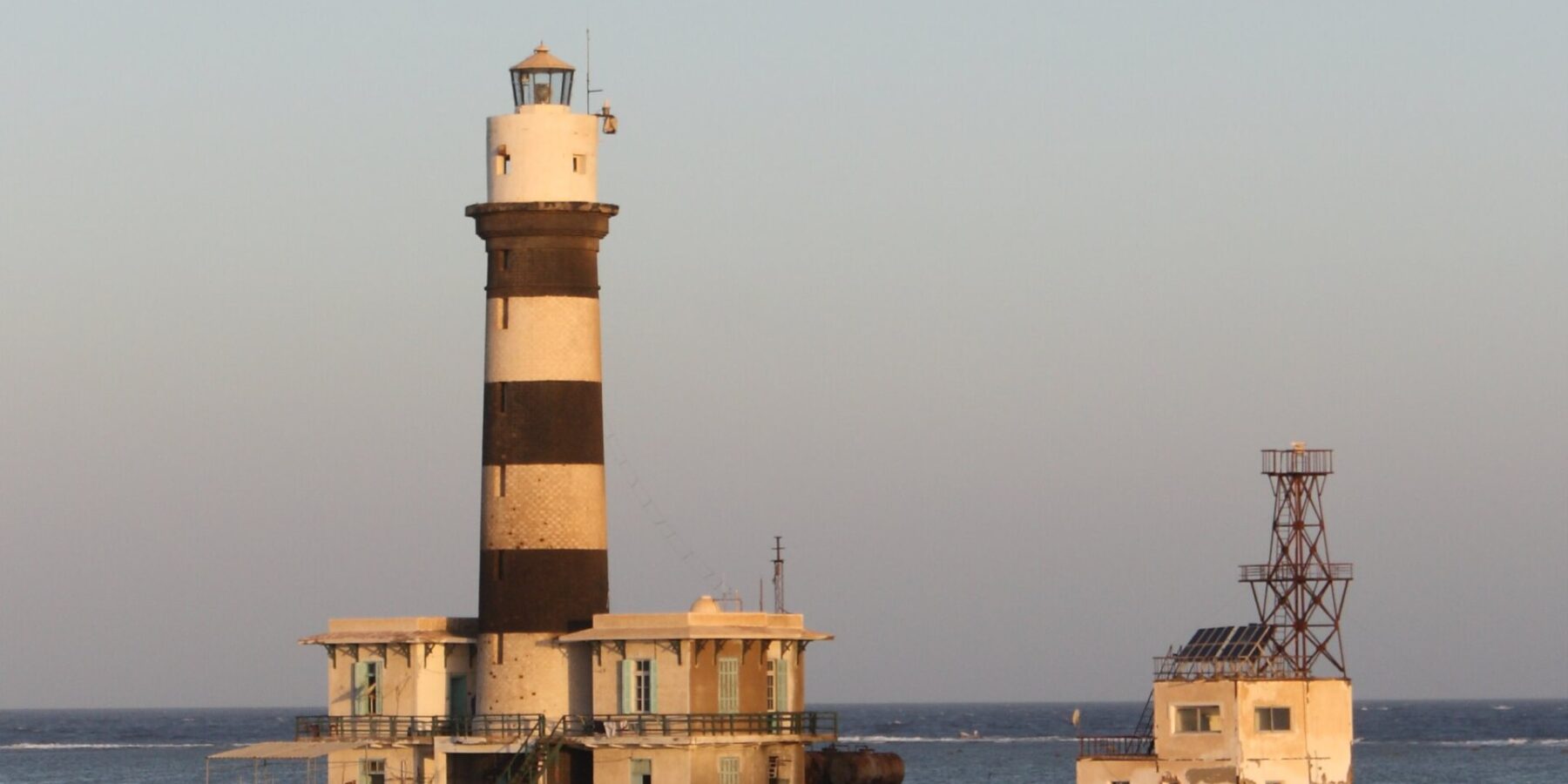 Le phare de Daedalus, une tour à bandes noires et blanches posée sur le récif, avec ses bâtiments et sa jetée métallique, au coucher du soleil