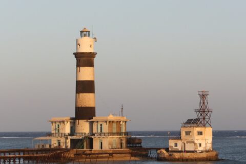 Le phare de Daedalus, une tour à bandes noires et blanches posée sur le récif, avec ses bâtiments et sa jetée métallique, au coucher du soleil