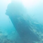 La poupe brisée du Thistlegorm dressée et inclinée dans le bleu, un plongeur sur la droite