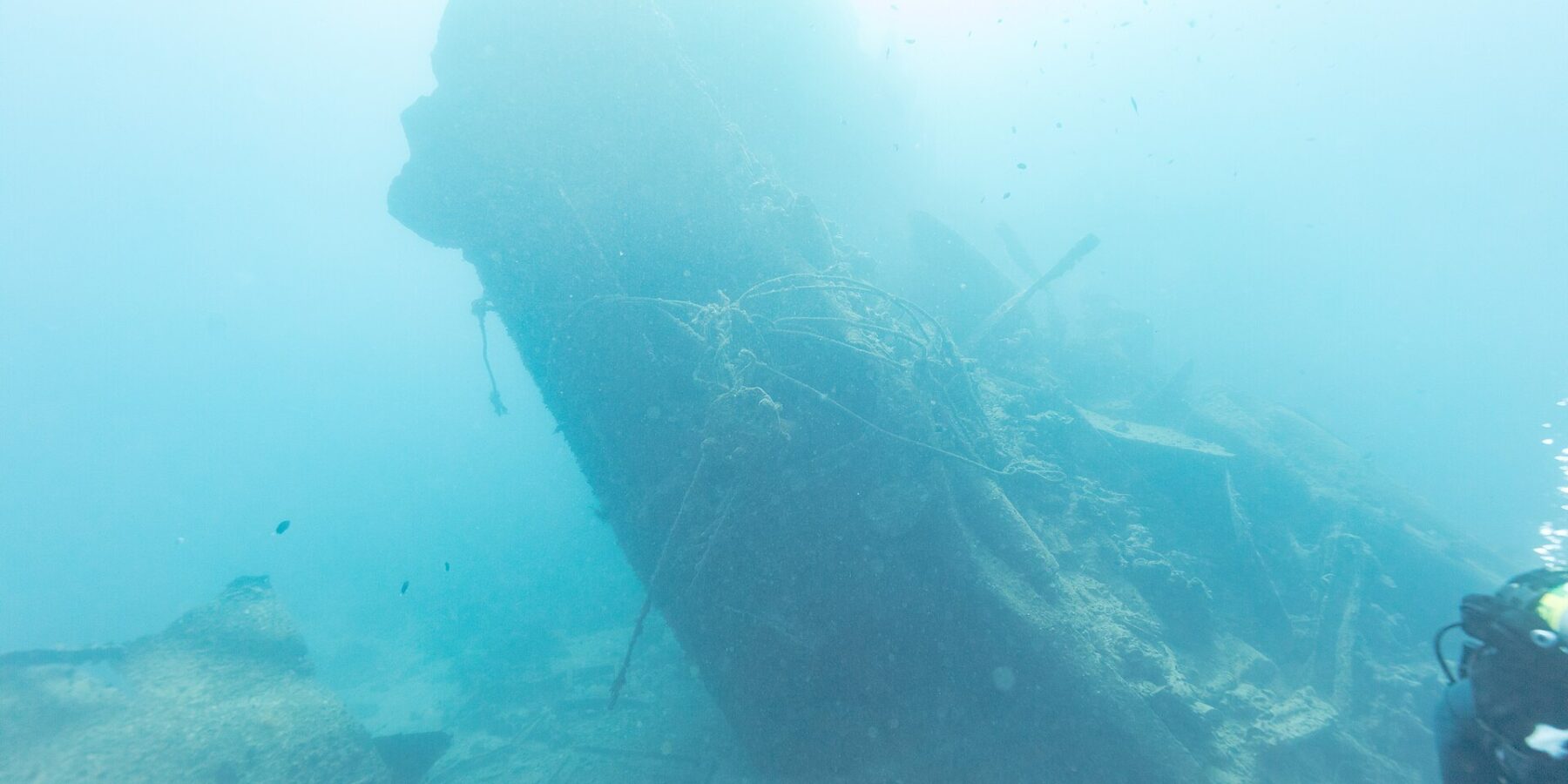La poupe brisée du Thistlegorm dressée et inclinée dans le bleu, un plongeur sur la droite