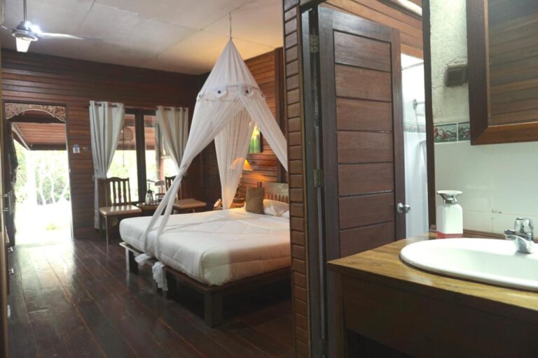 Une chambre au grand lit sous moustiquaire, avec un lavabo au premier plan