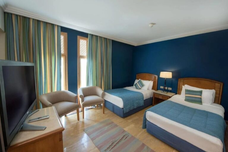Une chambre à deux lits aux murs bleus, avec deux fauteuils devant les fenêtres