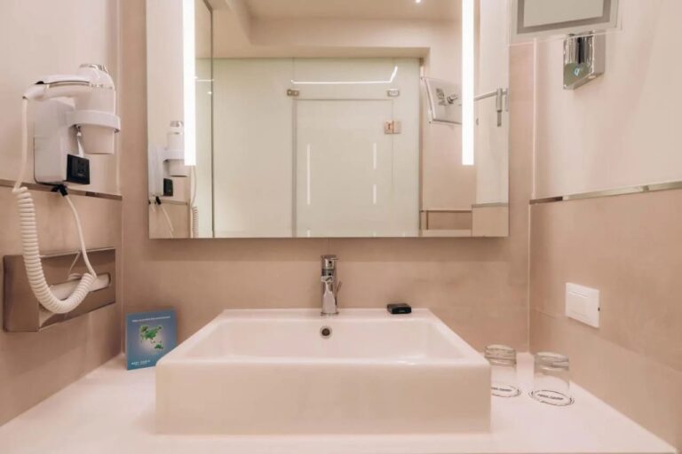 Une vasque blanche sous un miroir éclairé, avec un sèche-cheveux au mur
