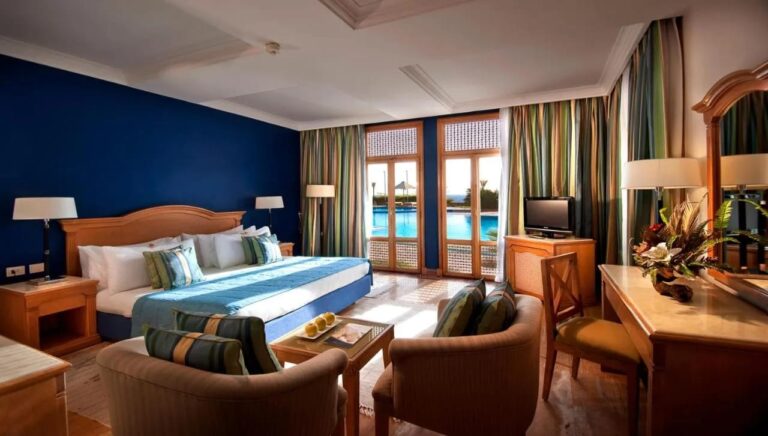 Une chambre au grand lit avec un mur bleu et des portes-fenêtres sur la piscine