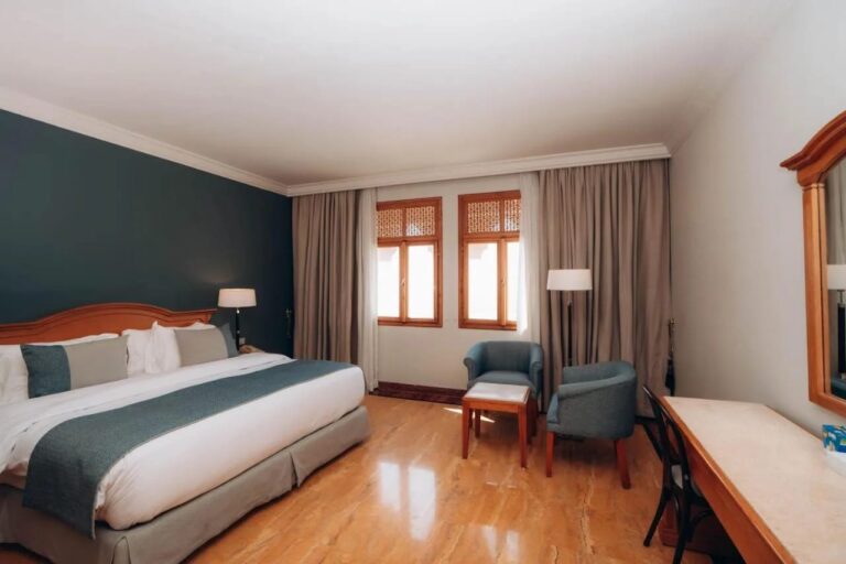 Une chambre au grand lit avec un mur vert sombre et deux fauteuils bleus