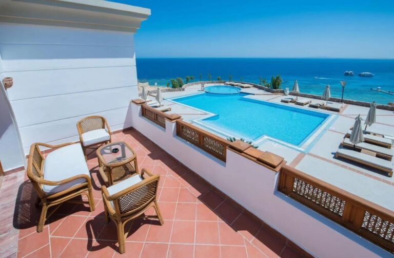 Une terrasse meublée en rotin au-dessus d'une grande piscine et de la mer Rouge, au Reef Oasis Beach Resort