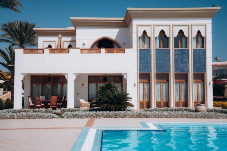 Un bâtiment blanc du Reef Oasis Beach Resort, aux fenêtres en arc et aux panneaux de mosaïque bleue, devant une piscine