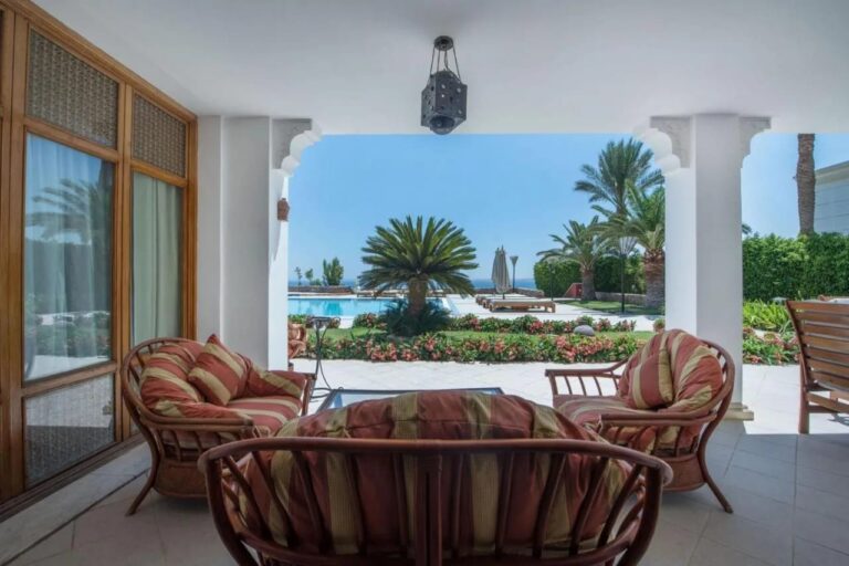 Une terrasse couverte meublée en rotin, face au jardin fleuri, à une piscine et à la mer