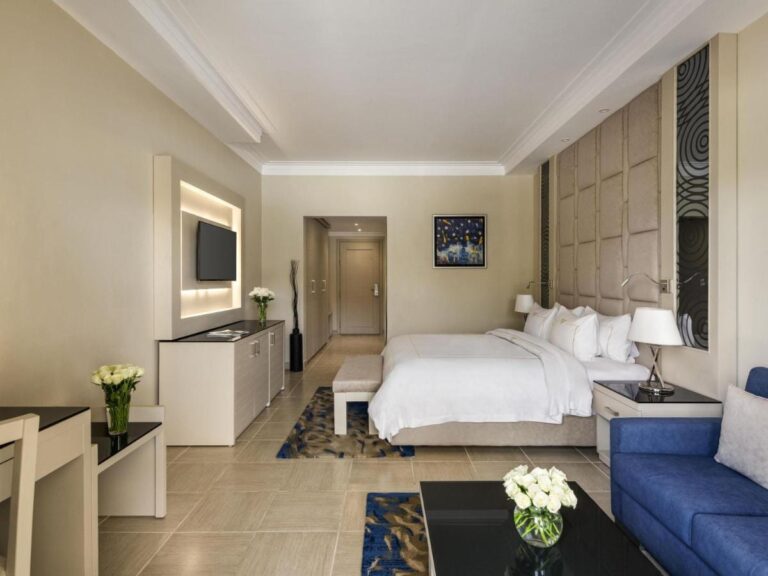 Une chambre au grand lit, avec un canapé bleu et des fleurs blanches sur la table