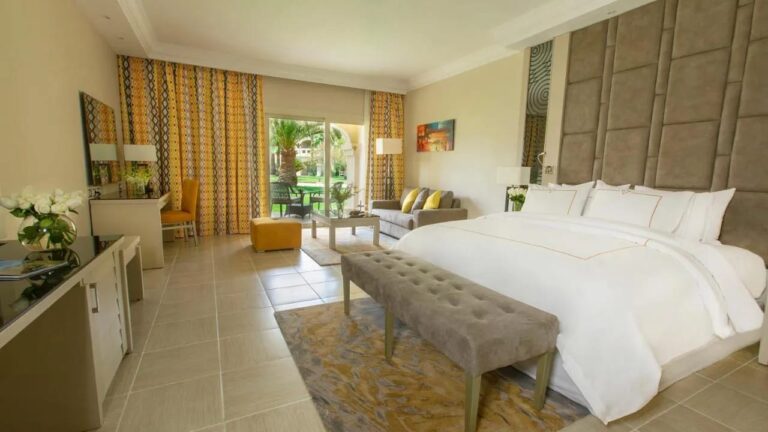 Une chambre au grand lit ouverte sur le jardin, avec une banquette au pied du lit