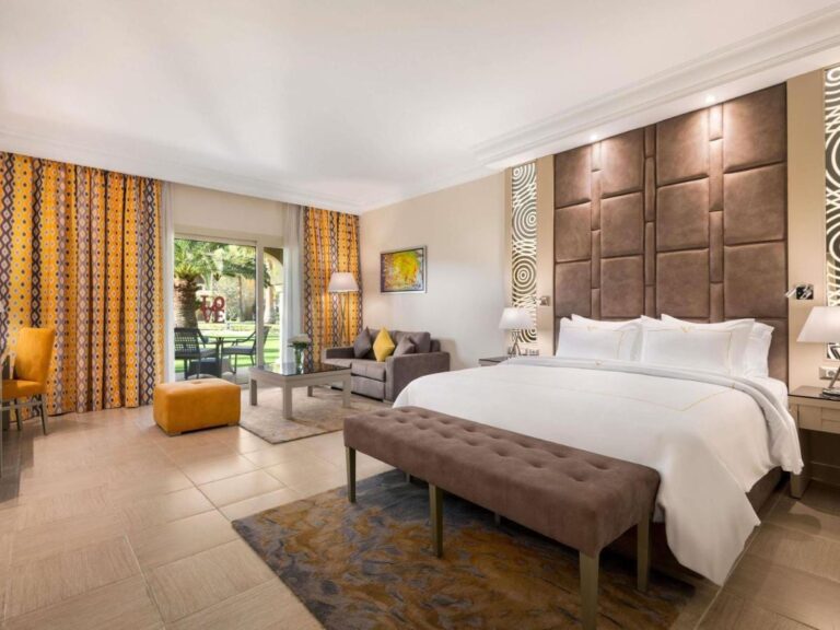Une chambre au grand lit avec un coin salon et une porte-fenêtre sur le jardin