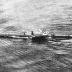 Photo d'archives en noir et blanc, prise d'avion, d'un sous-marin qui file en surface sur une mer ridée, sillage le long de la coque et kiosque au centre.