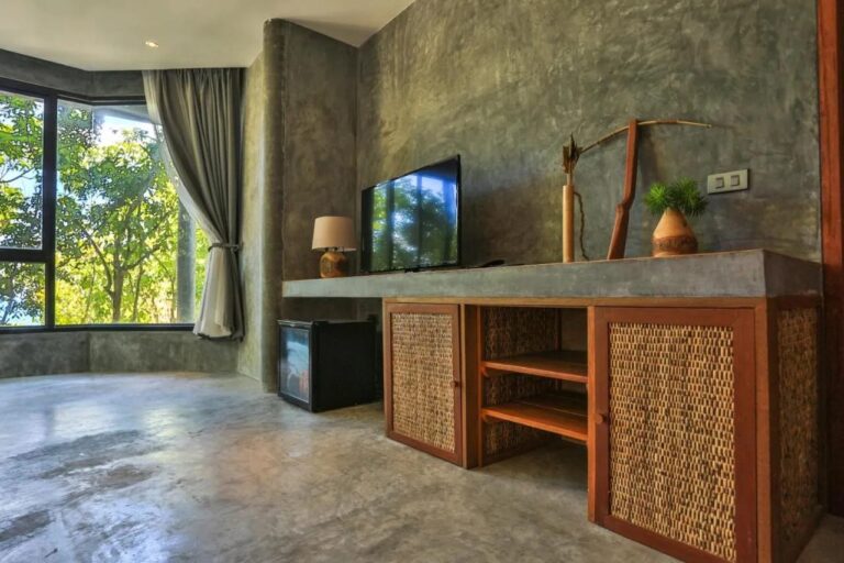 Une télévision sur un meuble en bois et rotin, près d'un minibar et d'une baie vitrée