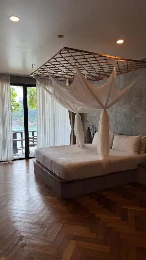 Une chambre au parquet en chevrons, avec un lit sous moustiquaire et une porte vitrée sur la mer