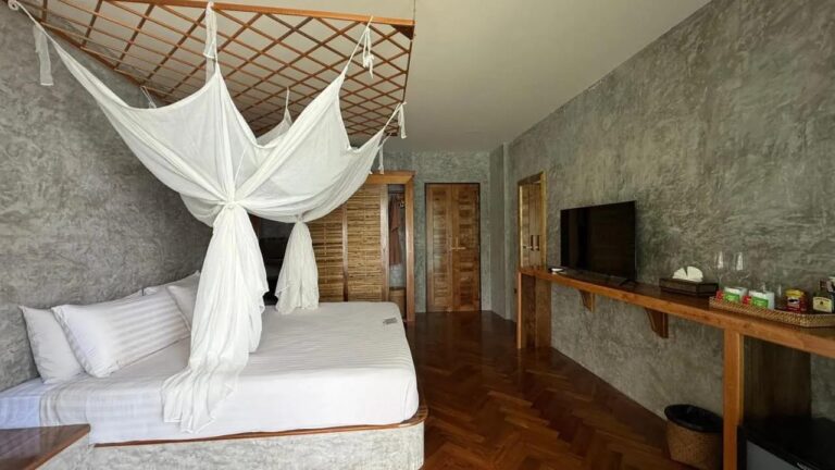 Une chambre au parquet en chevrons, avec un lit sous moustiquaire, une télévision et un coin thé