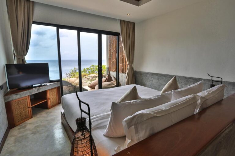 Une chambre du Sai Daeng Resort avec une baie vitrée sur la mer et les rochers