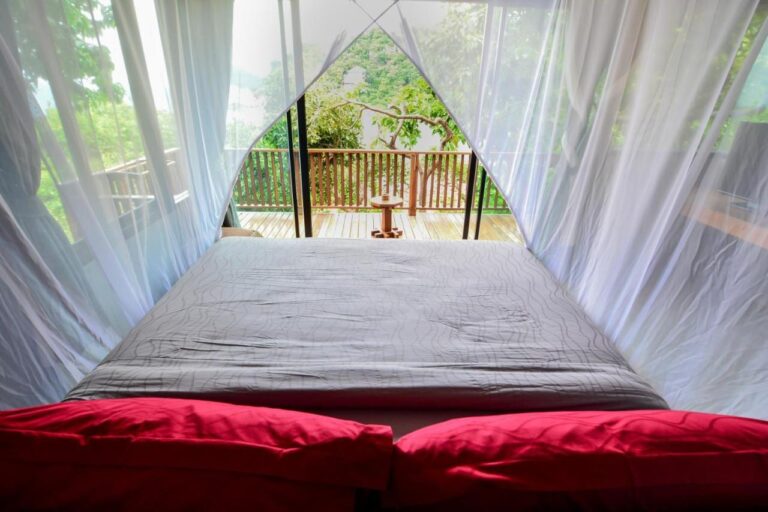 Vue depuis le lit, à travers la moustiquaire, sur une terrasse en bois et les arbres