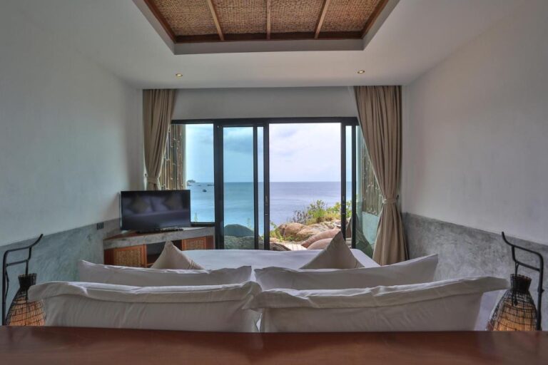 Une chambre face à la mer, vue depuis la tête du lit, avec deux lampes en osier