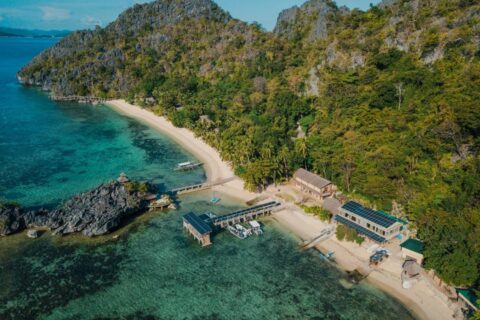 Vue aérienne du Sangat Island Dive Resort, sa plage, sa jetée et ses bateaux, au pied des falaises