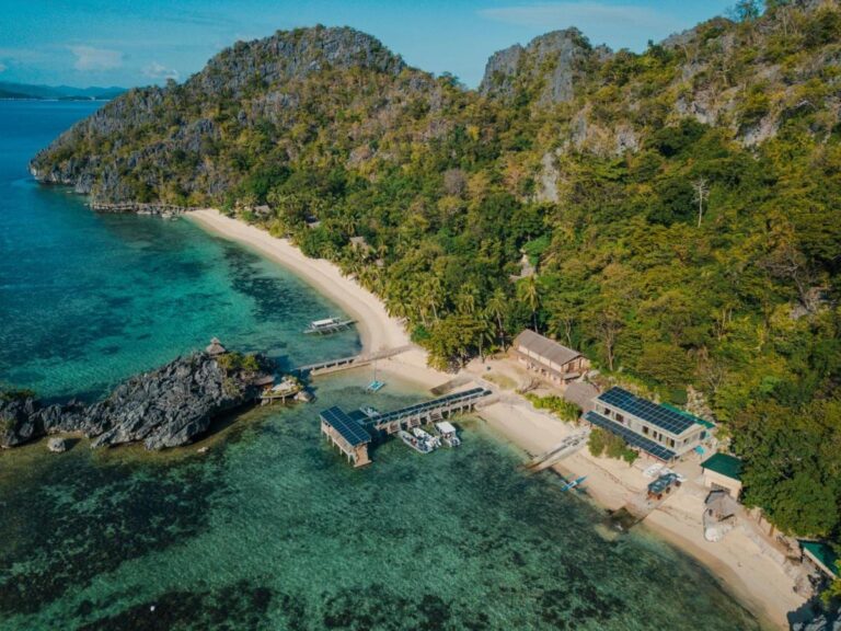 Vue aérienne du Sangat Island Dive Resort, sa plage, sa jetée et ses bateaux, au pied des falaises