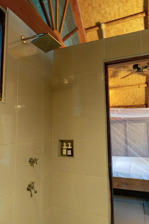 Une douche carrelée, ouverte sur la chambre et son lit sous moustiquaire
