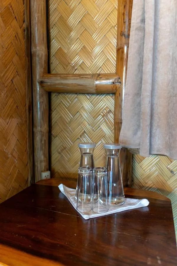 Deux carafes d'eau et des verres sur une table en bois, contre un mur en bambou tressé