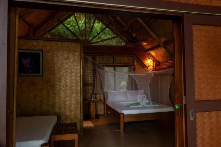 Une chambre aux murs en bambou tressé, avec un lit double sous moustiquaire et un lit simple