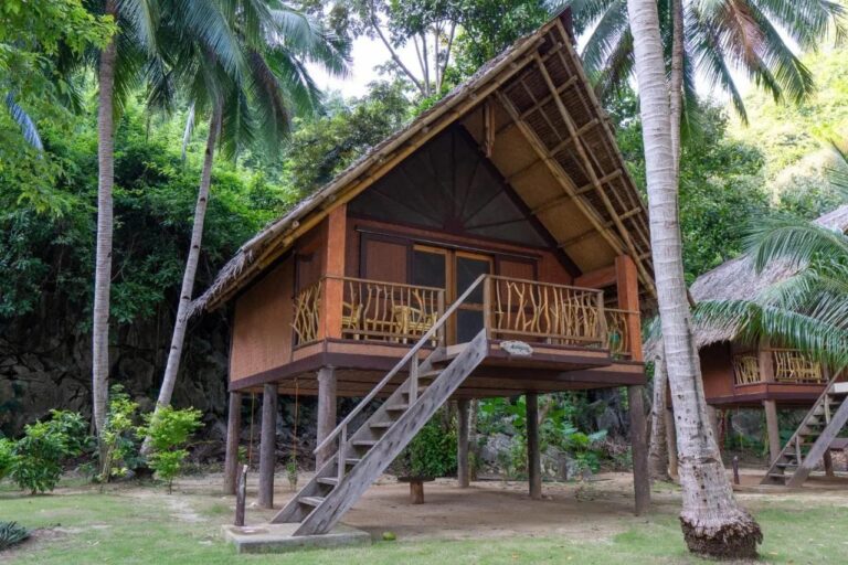 Un bungalow sur pilotis du Sangat Island Dive Resort, avec un escalier en bois, sous les palmiers