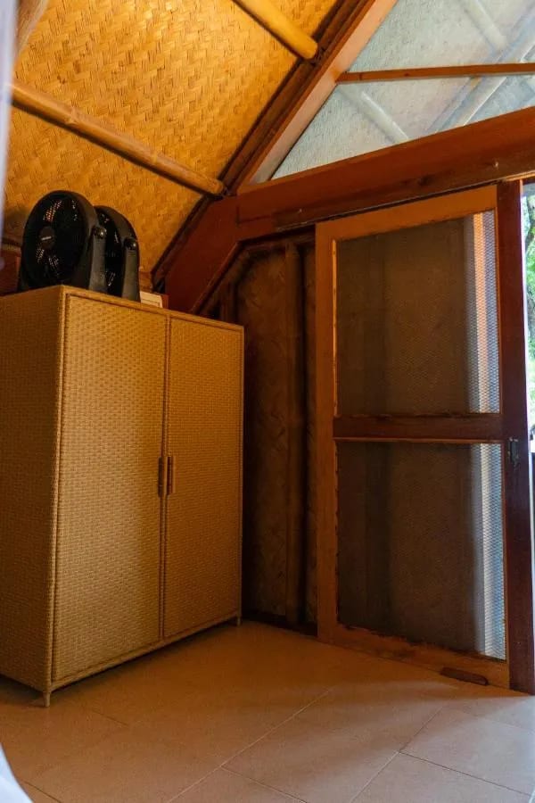 Une armoire tressée surmontée de deux ventilateurs, à côté d'une porte moustiquaire