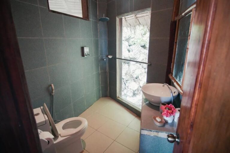 Une salle de bains carrelée de vert foncé, avec une vasque, une douche et une fenêtre sur les rochers