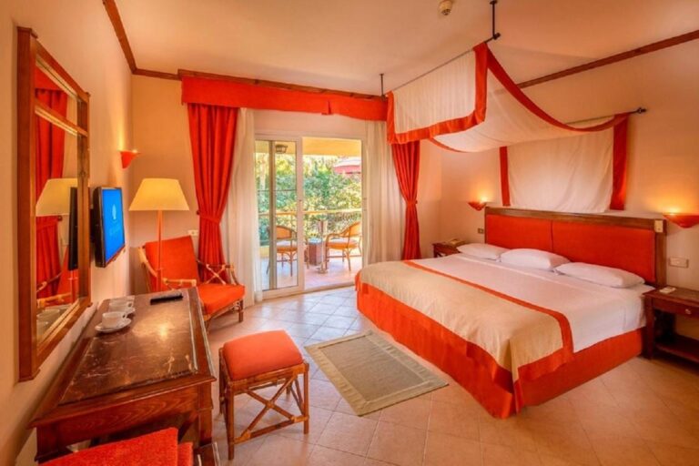 Une chambre au grand lit sous un ciel de lit blanc et orange, ouverte sur un balcon
