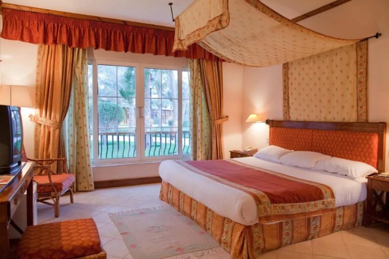 Une chambre au grand lit sous un ciel de lit fleuri, avec une baie vitrée sur le jardin