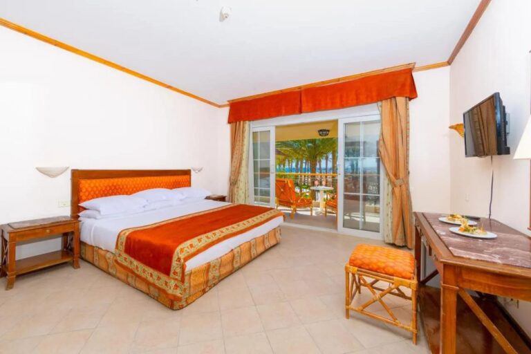 Une chambre au grand lit ouverte sur un balcon, avec les palmiers et la mer au fond