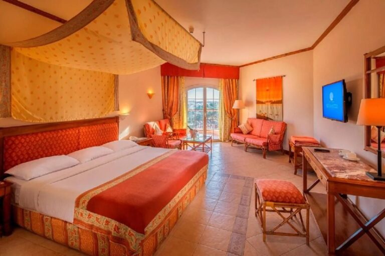 Une grande chambre avec un lit sous un ciel de lit, un canapé orange et un bureau