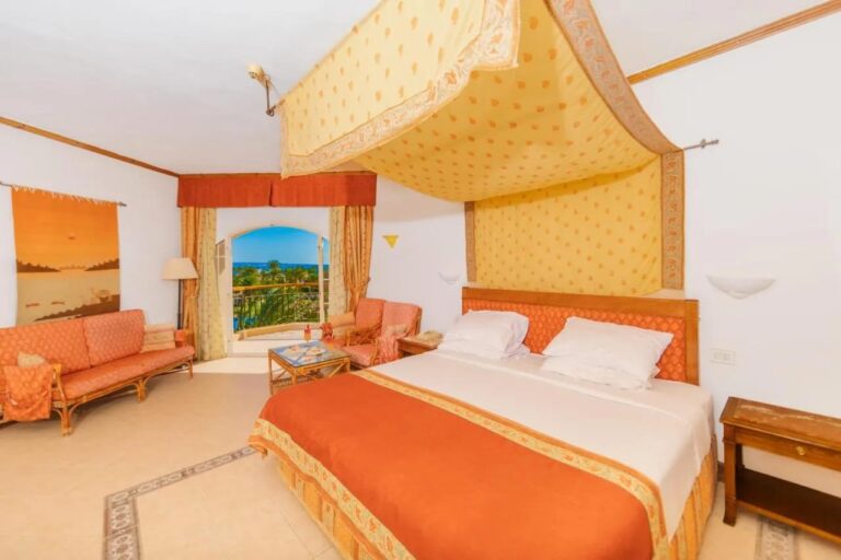 Une chambre du Siva Grand Beach avec un grand lit sous un ciel de lit jaune, un salon orange et la mer au loin
