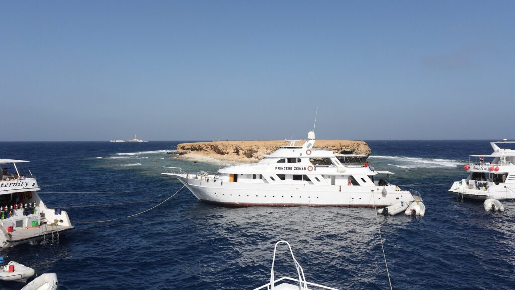 Trois bateaux de croisière amarrés devant l'îlot plat de Small Brother, le phare de Big Brother visible à l'horizon