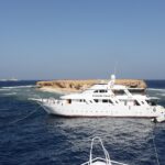 Trois bateaux de croisière amarrés devant l'îlot plat de Small Brother, le phare de Big Brother visible à l'horizon