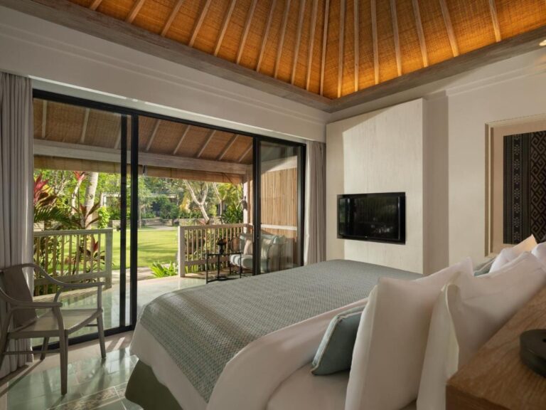 Une chambre sous un plafond en bois, ouverte sur une terrasse et la pelouse