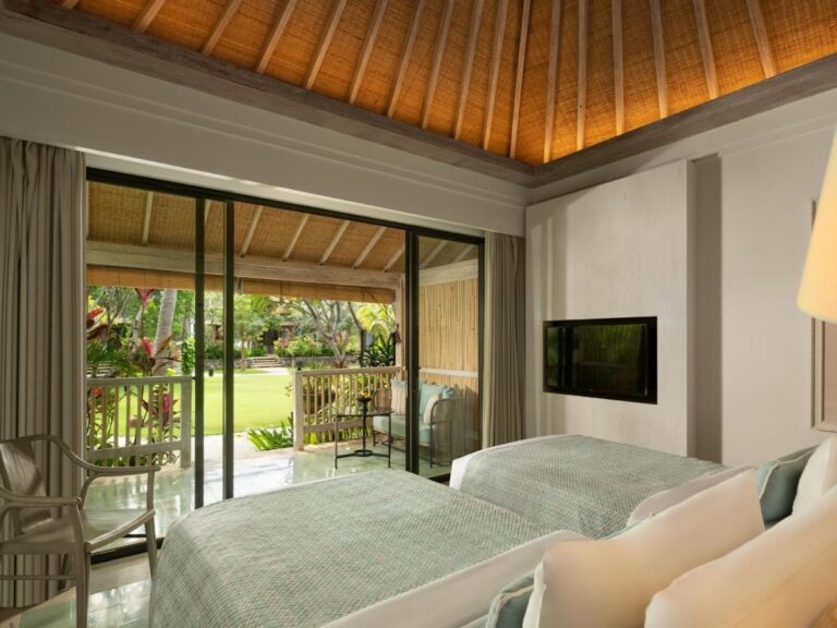 Une chambre à deux lits sous un plafond en bois, avec une baie vitrée sur le jardin