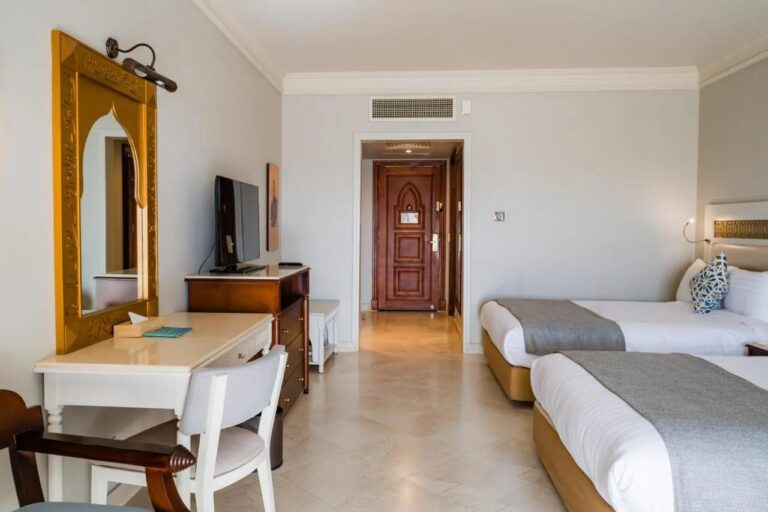 Une chambre à deux lits avec un bureau blanc et un miroir doré en forme d'arche