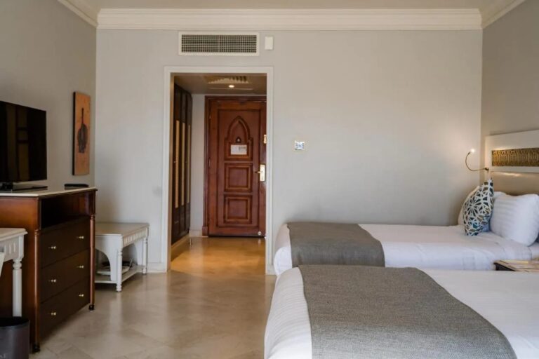 Deux lits face à une commode en bois et à la porte d'entrée sculptée