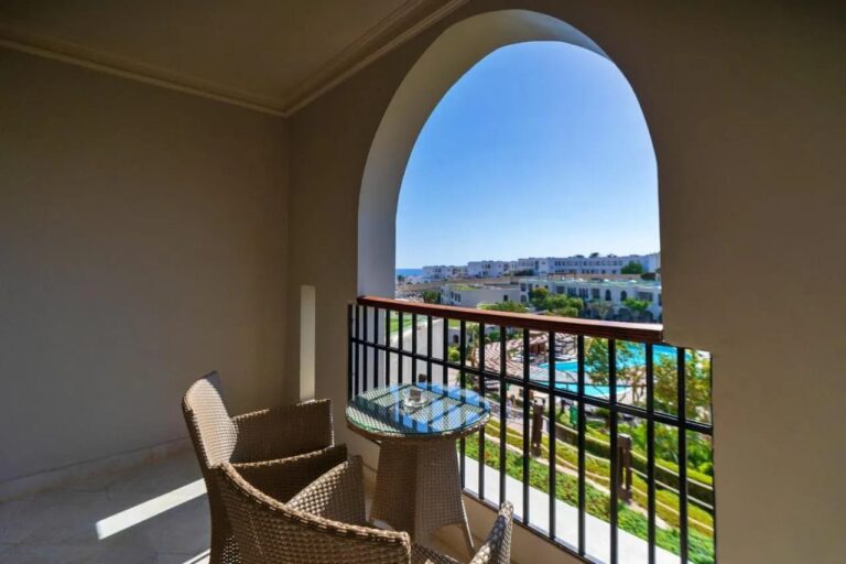 Un balcon sous une arche, avec deux fauteuils tressés, au-dessus des piscines et des jardins